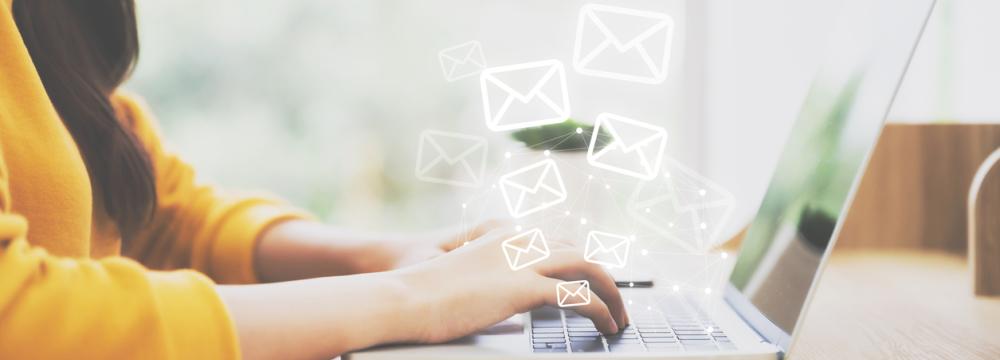 Une personne est assise à un bureau et tape sur un ordinateur portable , tandis que des icônes de courrier électronique numérique apparaissent au-dessus du clavier.