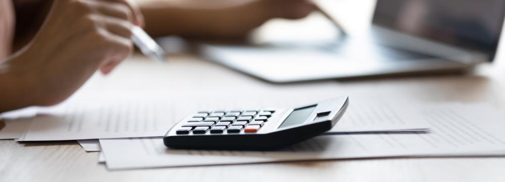 A person holding a pen pointed on a calculator and the other hand is scrolling on a laptop.