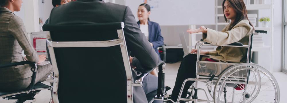People in business attire are seated in a circle, including a woman in a wheelchair.