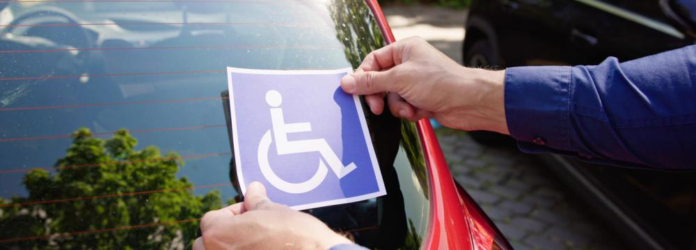 A person placing a blue disabled parking permit on the windshield of a car.