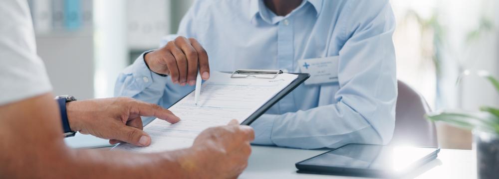 Un médecin montre une planchette avec des documents médicaux à un patient.