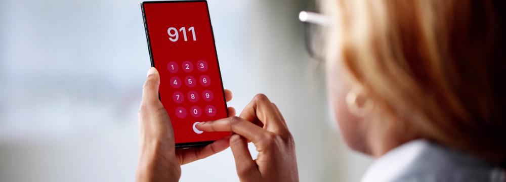 A woman holding a smartphone with "911" dialed on the screen.