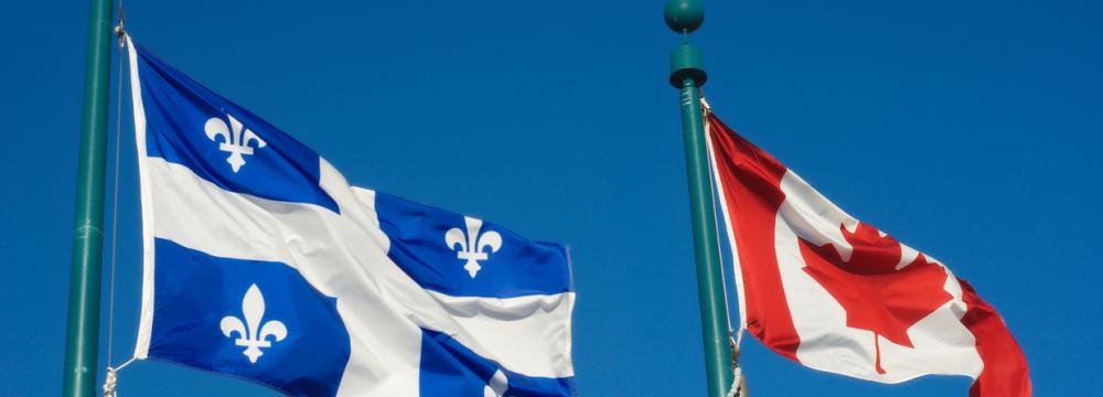 Quebec flag and Canadian flag flying side by side against a clear blue sky.